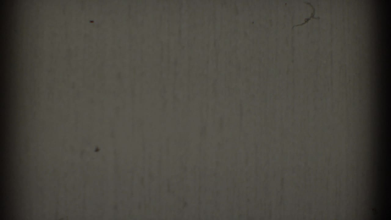 1969 Clarendon Hills 8mm frame with a blank gray-white surface, central dark band, soft edge falloff, and scattered film specks.