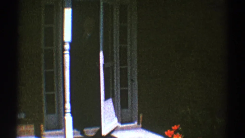 1969 Clarendon Hills 8mm frame showing the open white screen door, porch post, dark doorway, and red flowers near the lower edge.