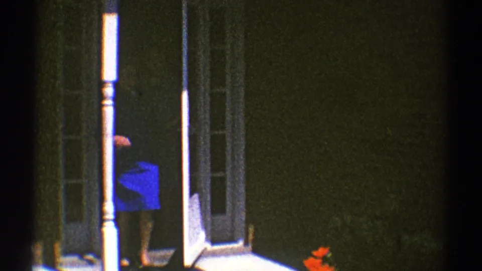 1969 Clarendon Hills home-movie frame showing a woman in blue partly visible near an open house doorway and white porch trim.