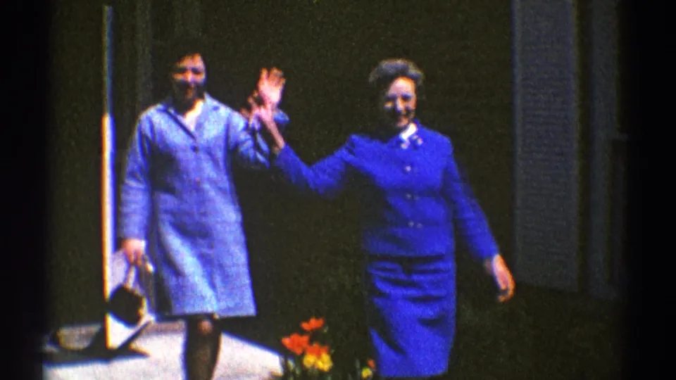 In a 1969 Clarendon Hills porch scene, two women in blue walk forward while one gives a casual wave.