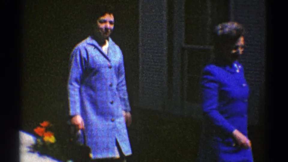 Late in the 1969 Clarendon Hills clip, one woman remains near the house while another in blue moves out of frame.