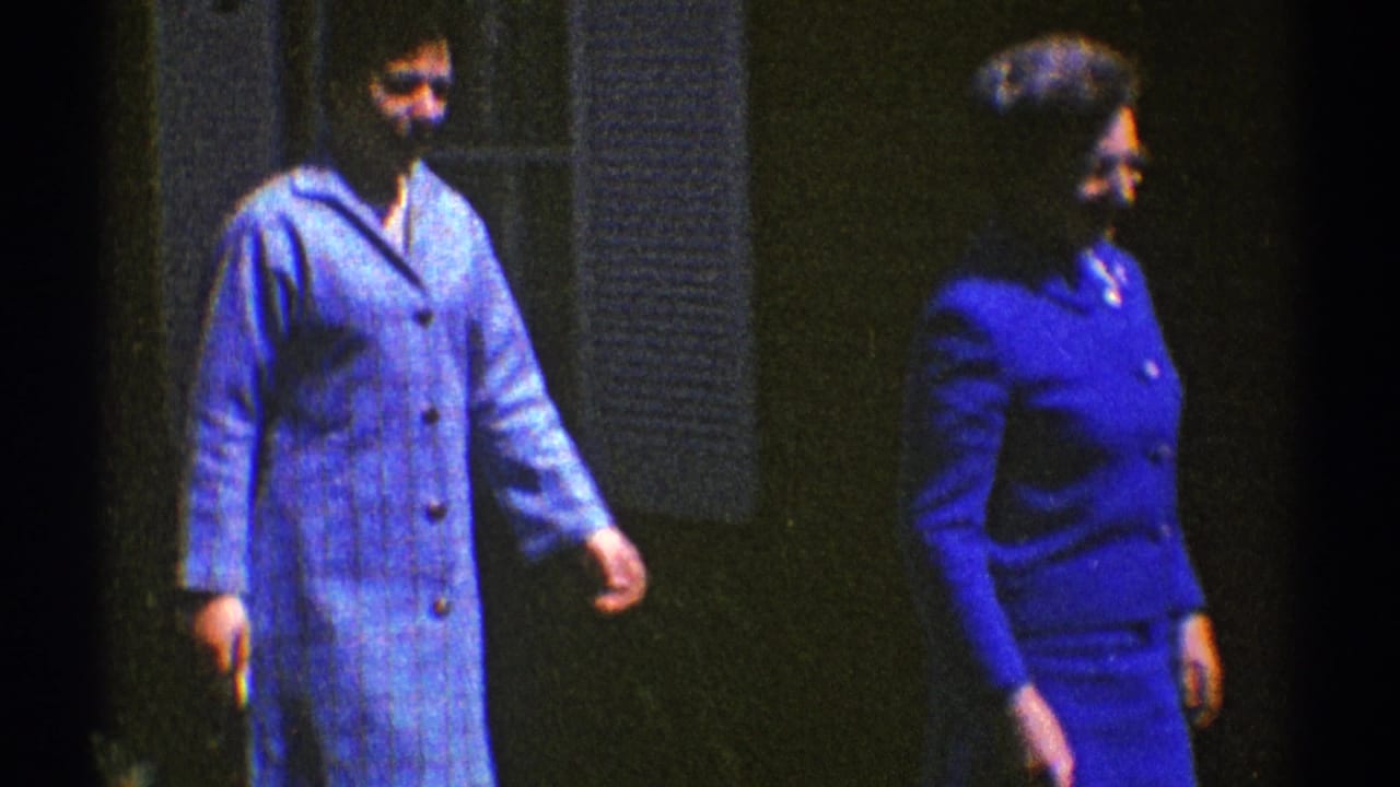 Two women in blue clothing walk beside a dark exterior wall.