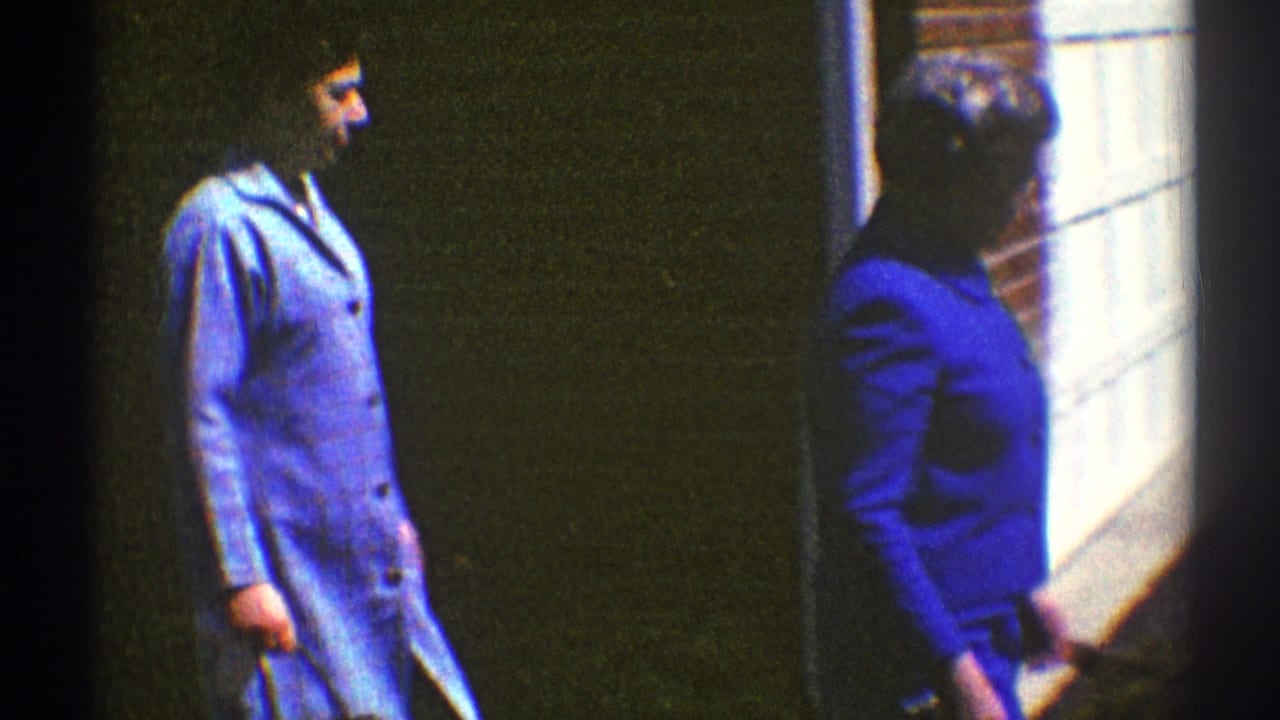 The women continue walking past a brick exterior and white garage door, with their blue garments and handbags visible.
