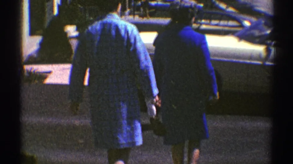 Seen from behind, the two women walk away across the driveway area near a parked car and white garage doors.