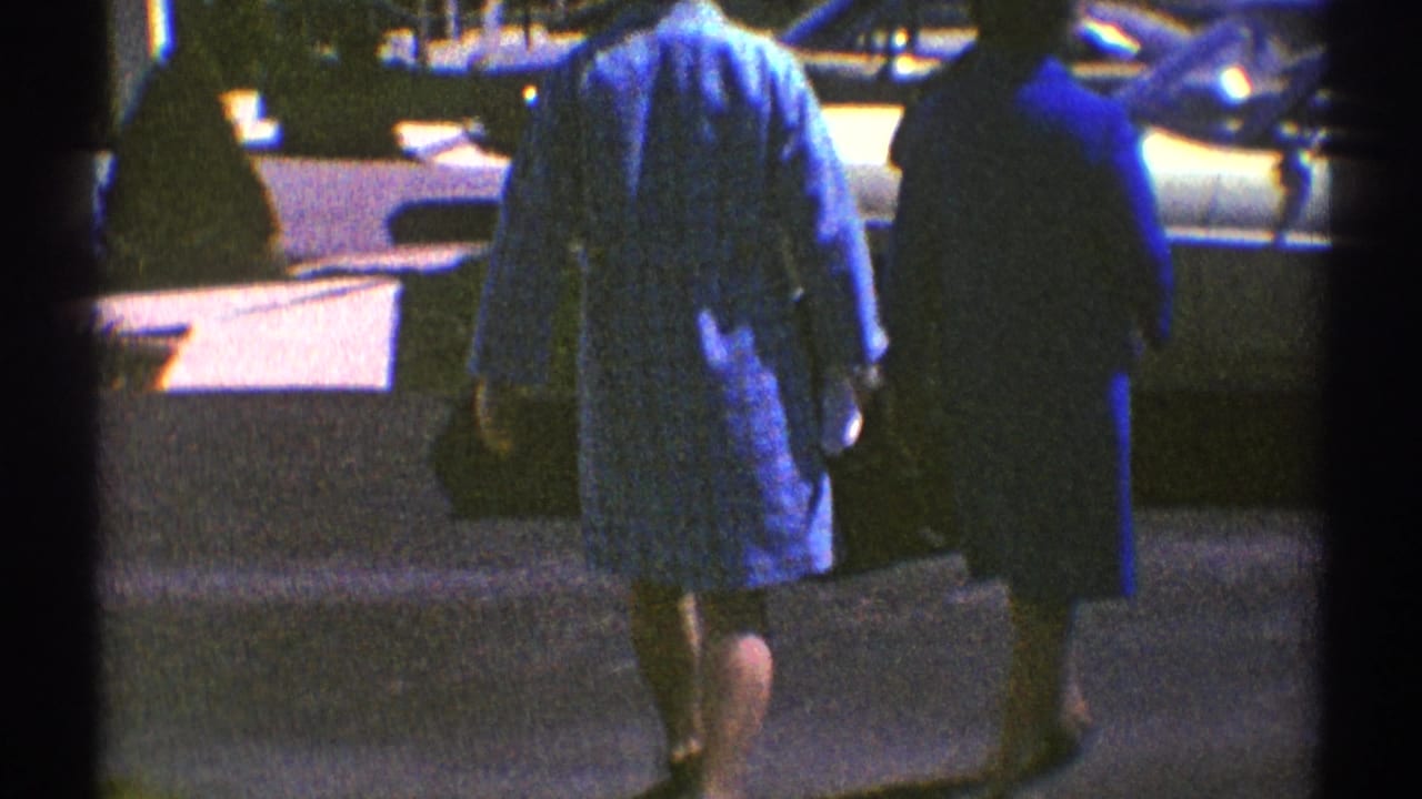Adults walk toward a light-colored sedan in bright sun, seen through 8mm film borders.