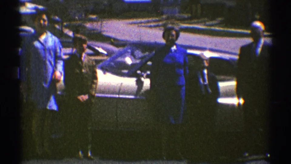 Adults stand beside the sedan in the closing frame of the 1969 Clarendon Hills home movie, with the car and street visible behind them.