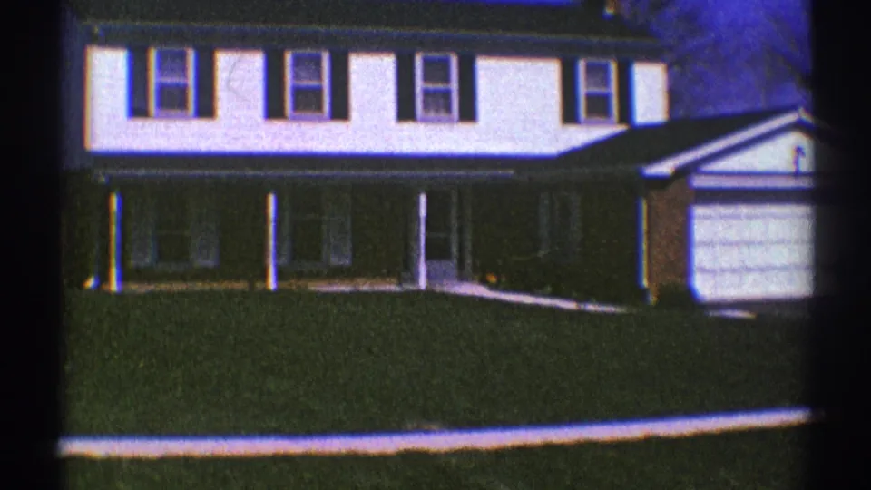 The 1969 8mm footage holds on a Clarendon Hills suburban house exterior with lawn, shutters, and garage.