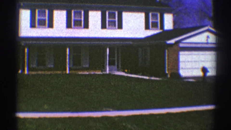 1969 Clarendon Hills home-movie frame showing a white two-story house, dark shutters, front porch, lawn, and garage.