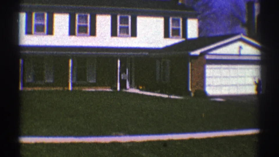1969 Clarendon Hills frame showing the suburban house exterior with a person visible near the front doorway and garage at right.