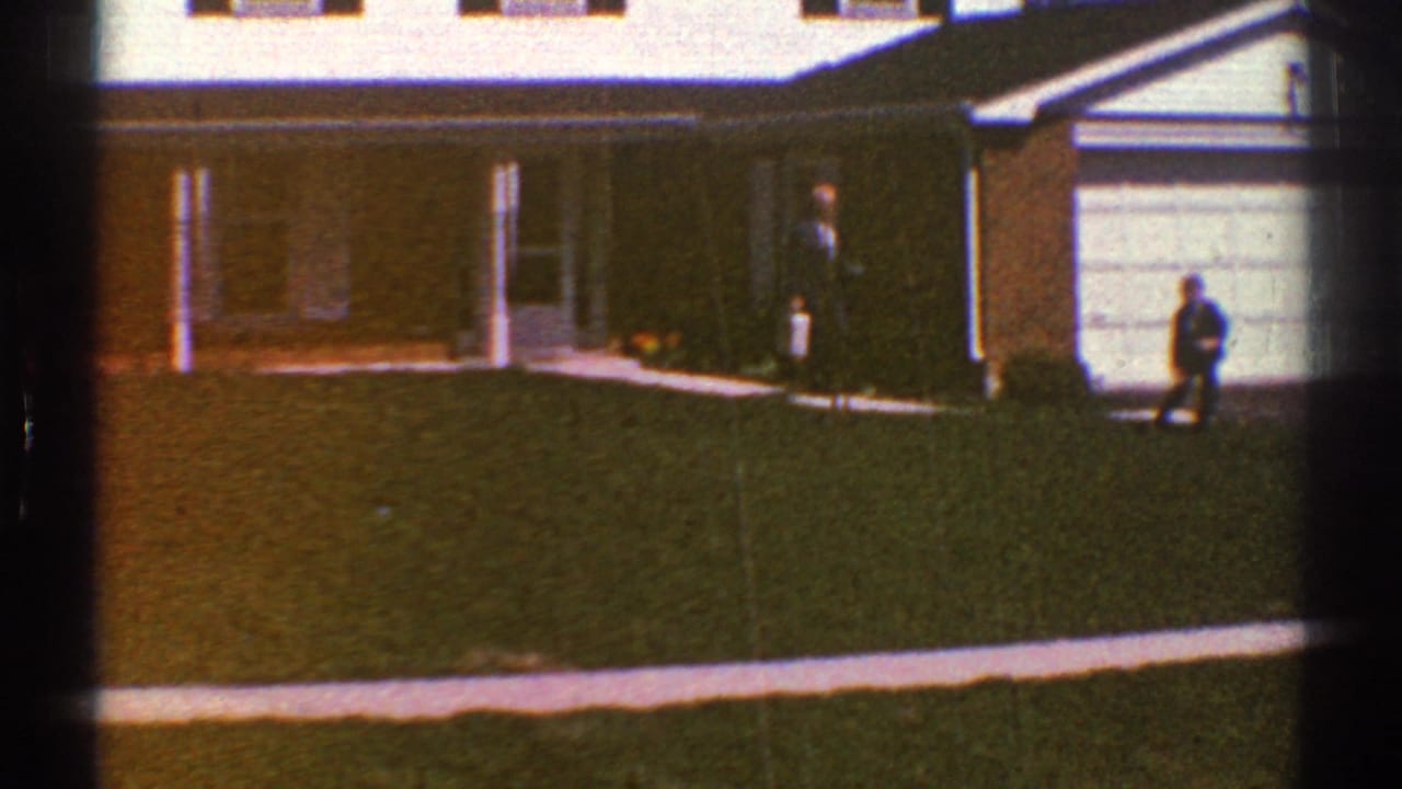 1969 Clarendon Hills home-movie frame showing a suburban house, green lawn, concrete walk, garage door, and two distant people.