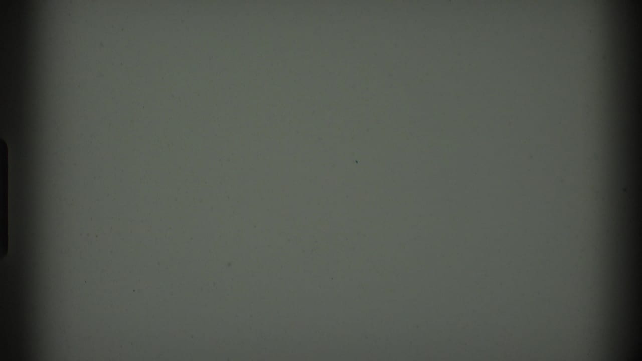 Blank or near-blank 8mm frame following the house scene, with dark gate edges, muted green-gray tone, and small dust marks.
