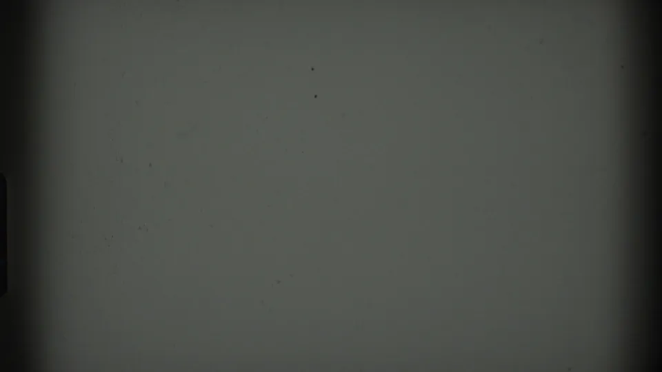Near-blank 8mm frame with dark film-gate borders, muted gray-green exposure, and scattered small specks from the reel.