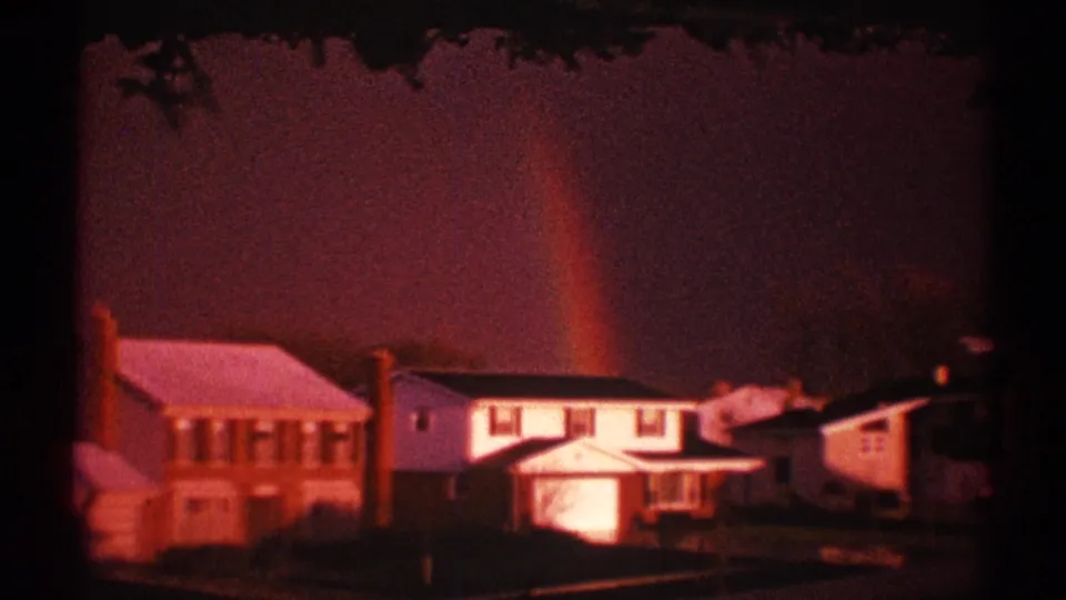 A 1969 Clarendon Hills home-movie frame shows houses along a residential street, dark trees, and a faint rainbow in the red sky.