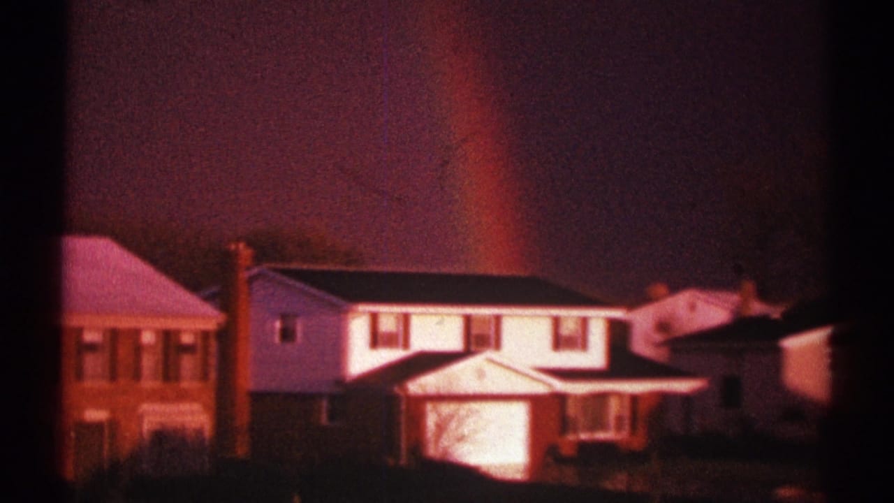 Rainbow over white and brick suburban houses under a dark sky.