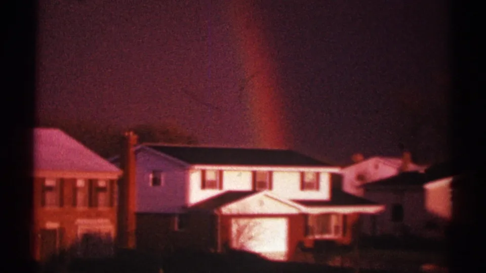 1969 Clarendon Hills home-movie frame showing a rainbow rising behind white and brick suburban houses.