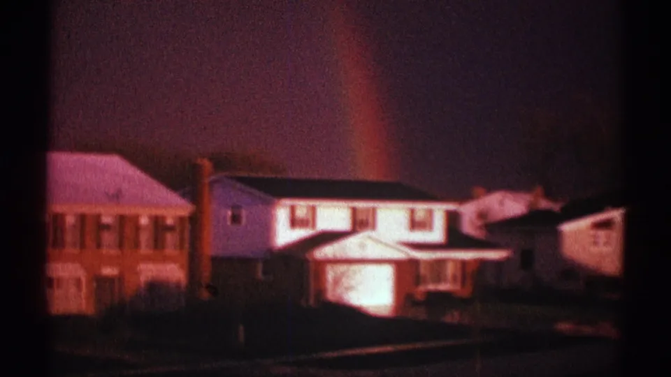Late clip frame from Clarendon Hills showing the rainbow behind residential houses and a darker street edge.