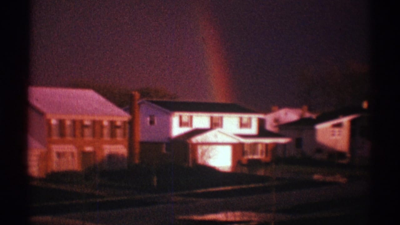 Rainbow over suburban houses beside a wet street after rain.