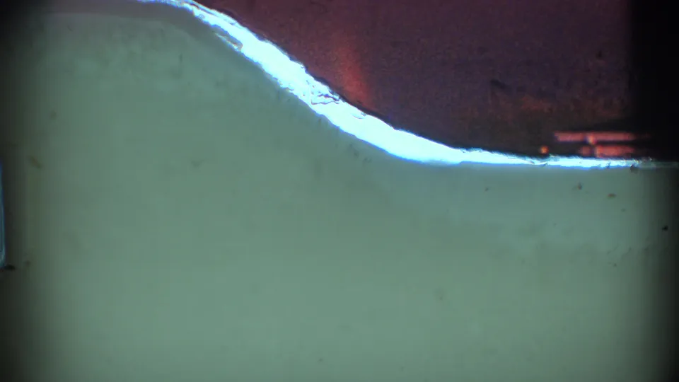 1969 8mm frame from the Clarendon Hills clip showing mostly dim color field, film-edge shadow, dust, and a bright curved edge at upper left.