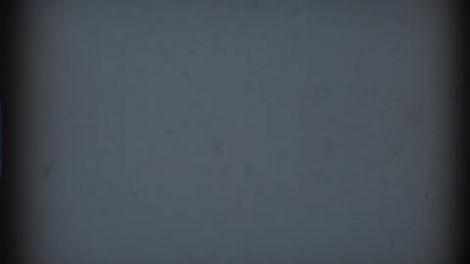 Low-light 8mm frame showing mostly soft gray-blue density, a dark vertical film edge, and scattered dust or emulsion marks.