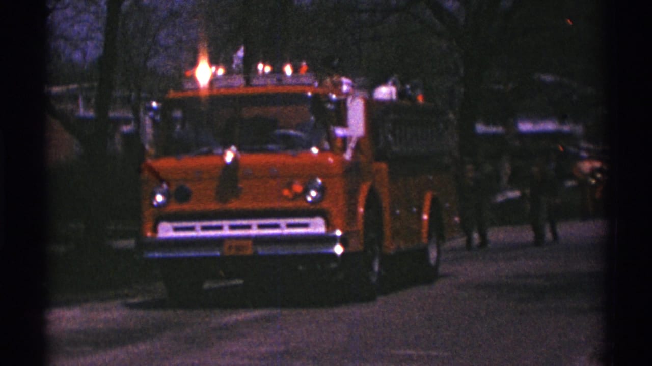 Orange fire truck passes closer with small figures and vehicles behind it.