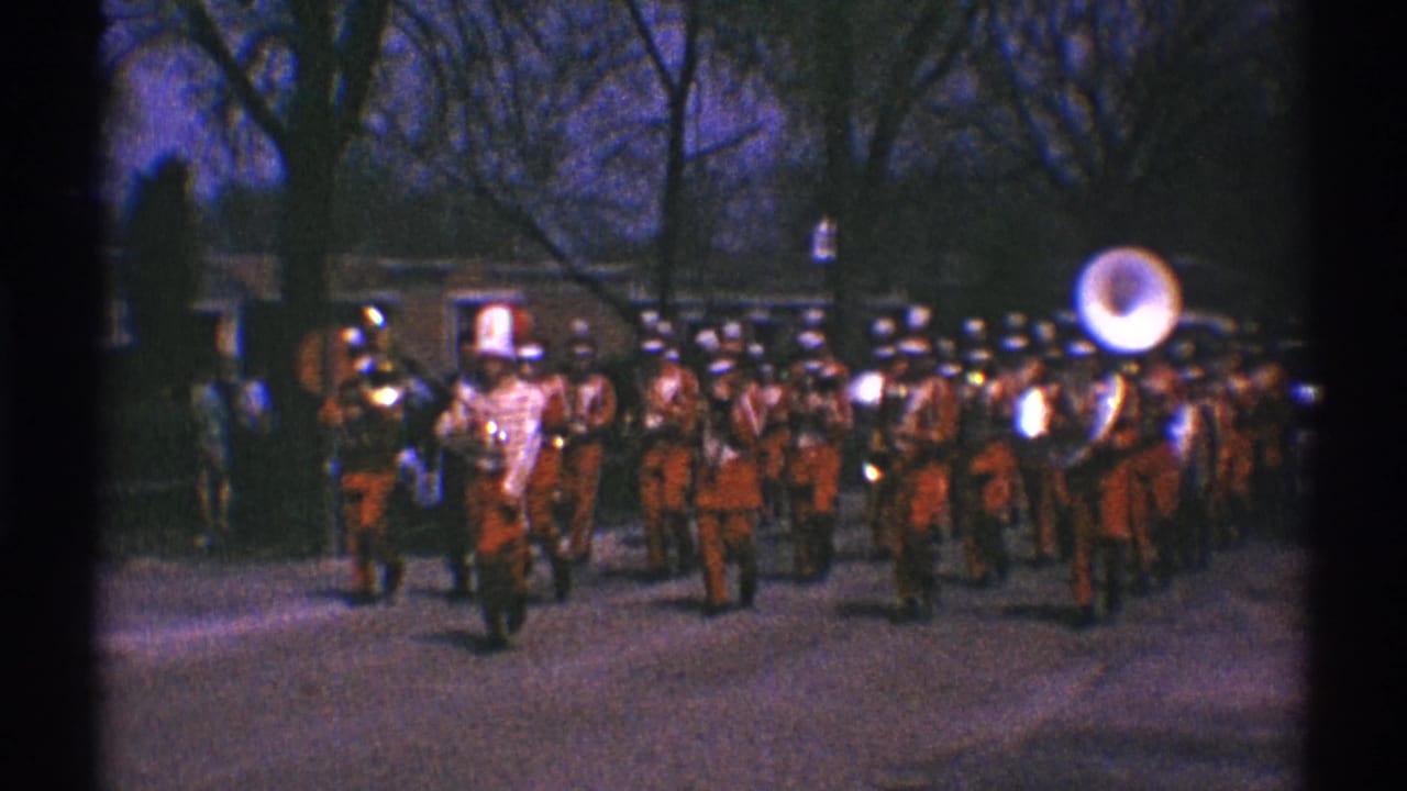 Marching band in red uniforms approaches along a residential street.