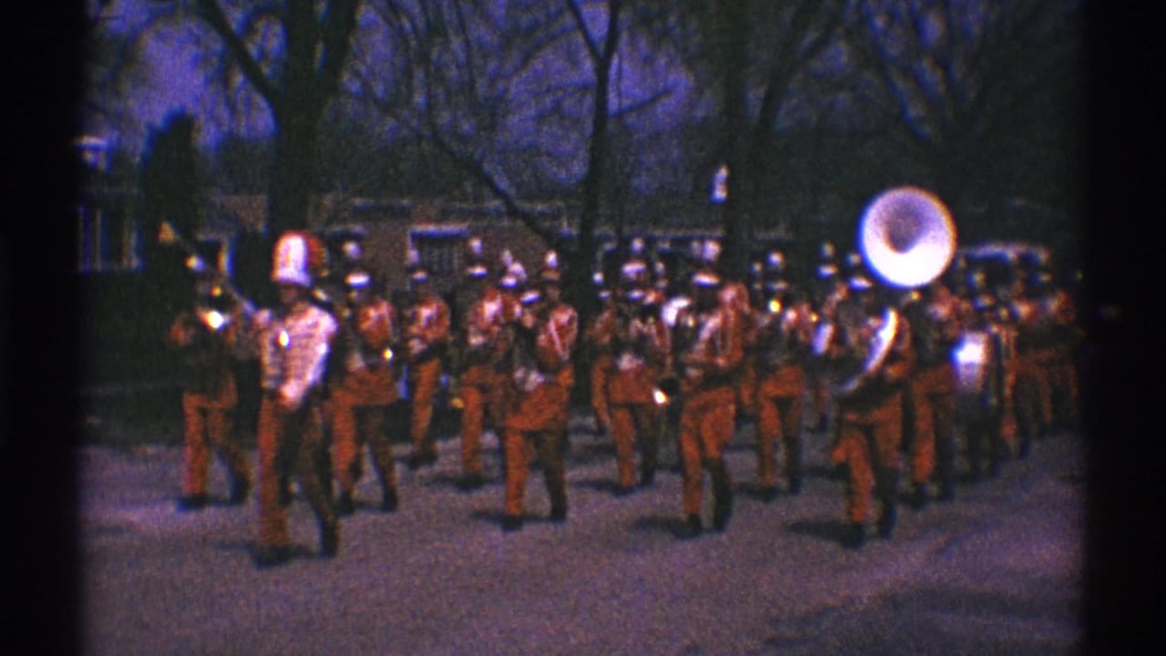 Red-uniformed marching band stands or marches with a large sousaphone at right.
