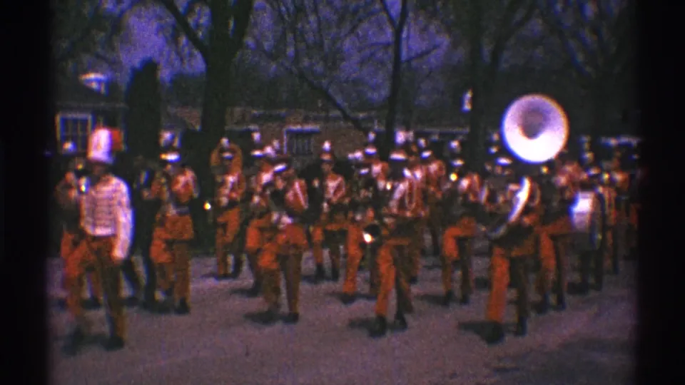 1969 Illinois parade frame showing red-uniformed musicians moving past the camera with brass instruments and a sousaphone.