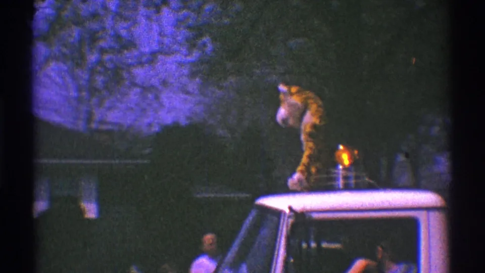 The tiger mascot remains on the white truck roof as the parade vehicle passes trees and spectators in Clarendon Hills, Illinois.
