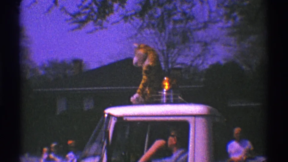 A tiger mascot stands on a white truck with people visible around the vehicle during the 1969 Clarendon Hills parade scene.