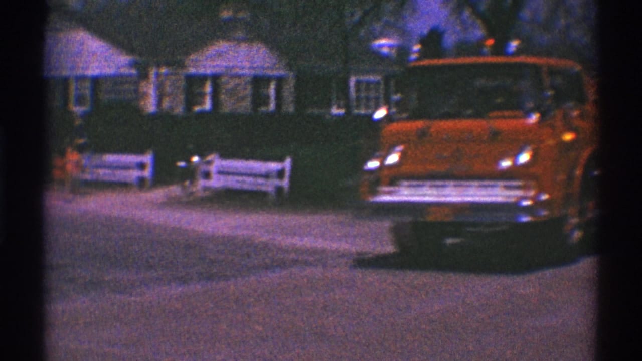 A red fire truck moves slowly through Clarendon Hills, Illinois, on 1969 8mm footage, passing houses, trees, and a white roadside fence.