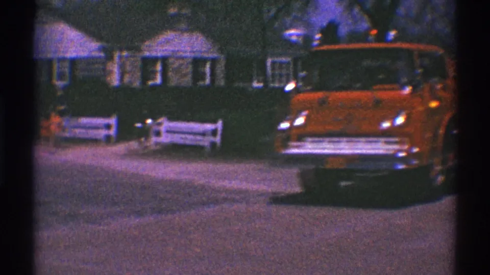 A red fire truck moves slowly through Clarendon Hills, Illinois, on 1969 8mm footage, passing houses, trees, and a white roadside fence.