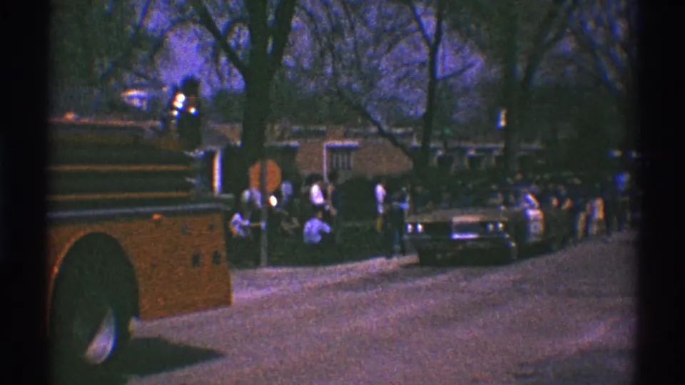 As the fire truck moves out of view, small groups of people stand near parked cars on a 1969 Clarendon Hills neighborhood street.