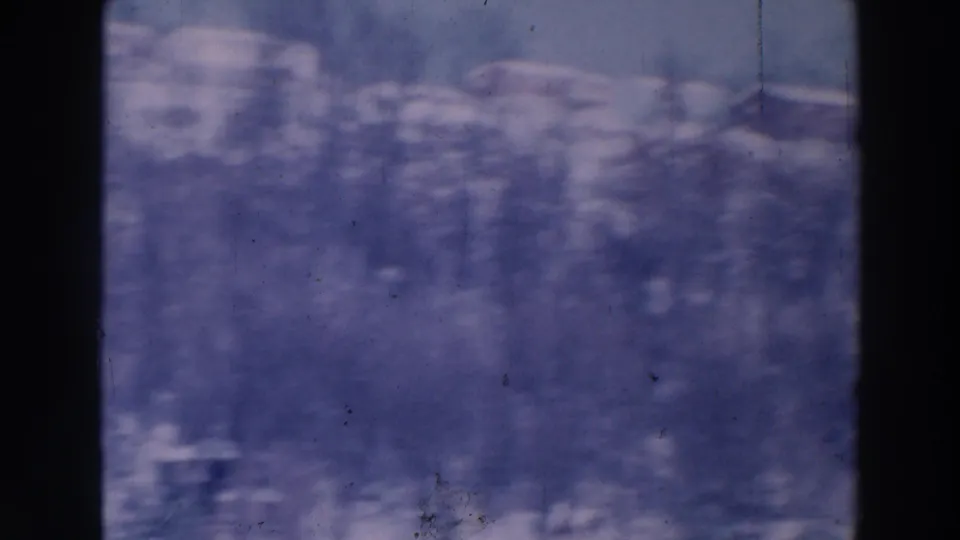 1964 Tustin, Wisconsin 8mm frame showing a hazy snowy landscape with bare trees and indistinct distant buildings.