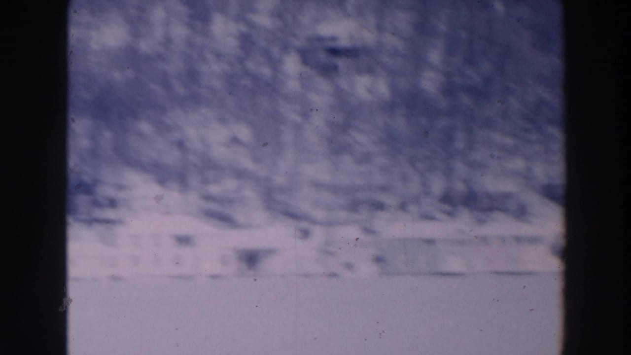 Snowy hillside with bare trees and faint white buildings, partly obscured by film softness.
