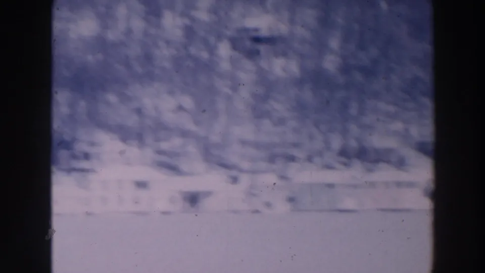 Hazy 1964 8mm view in Tustin, Wisconsin, with snow, winter trees, and pale buildings in the distance.