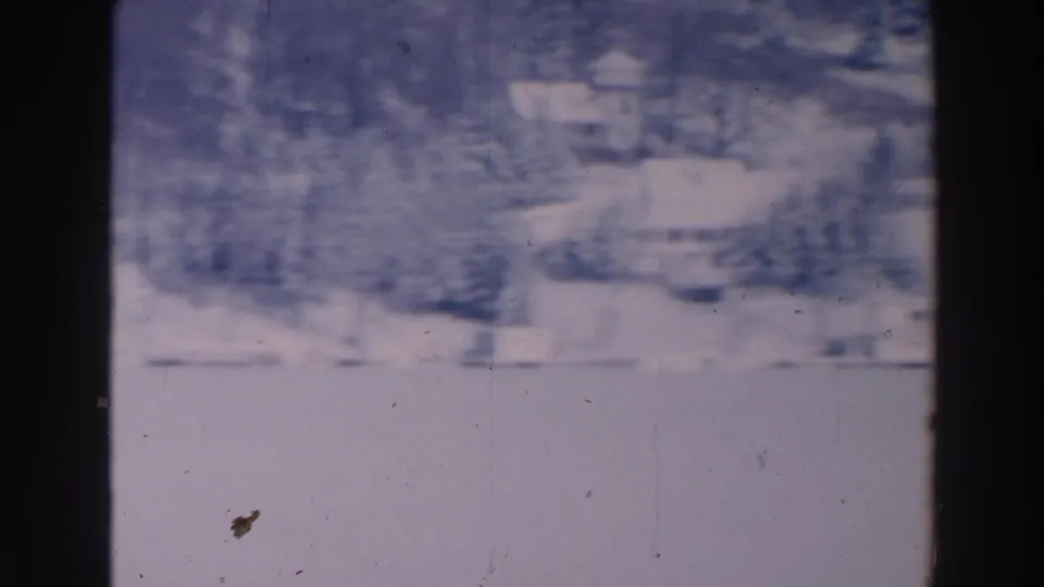 1964 Tustin, Wisconsin frame with distant buildings, snow cover, bare trees, and visible 8mm film grain.
