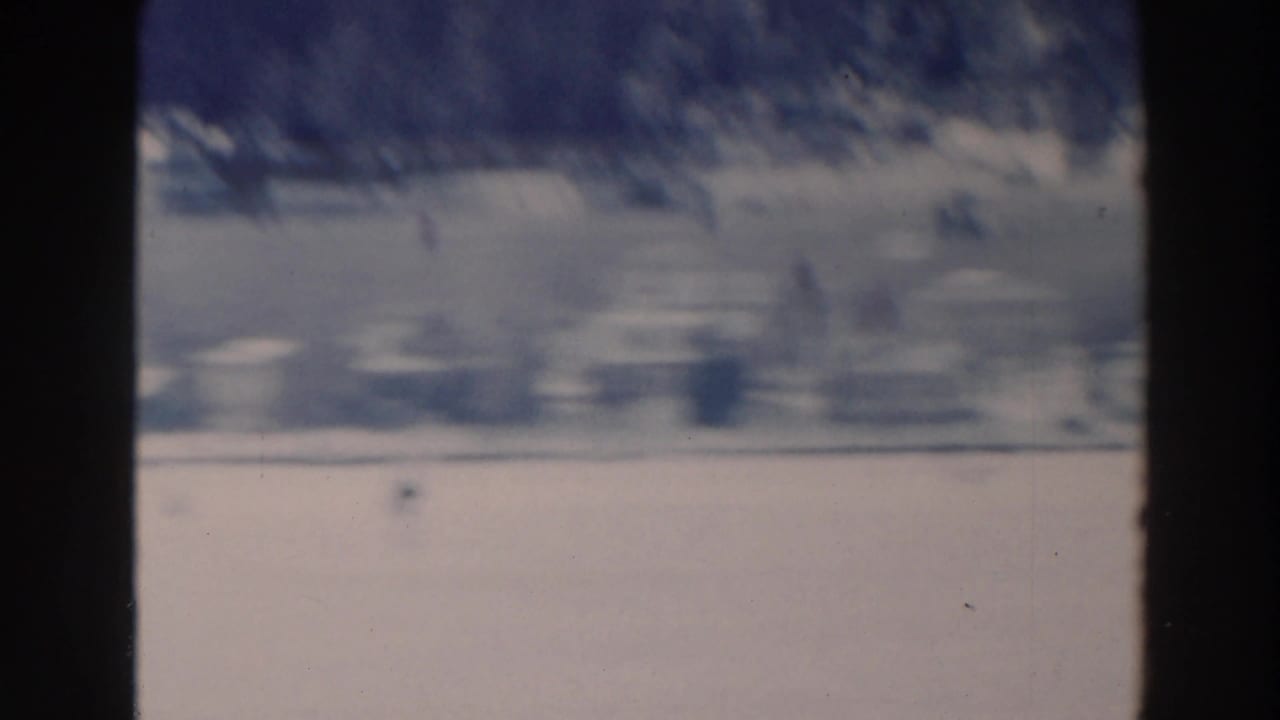 Soft, distant view across a frozen lake with a snowy shoreline and dark film borders.