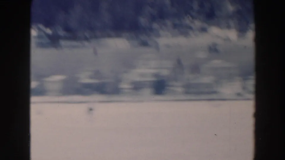 1964 8mm home-movie frame from Tustin, Wisconsin, showing a frozen lake and snowy shoreline through soft winter haze.