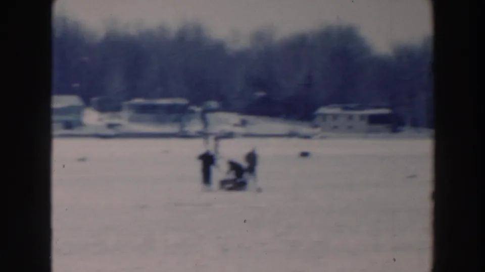 1964 Tustin, Wisconsin winter frame with bundled figures on a frozen lake and houses along the far shore.