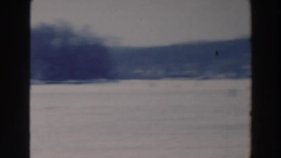 Wide 1964 8mm winter view in Tustin, Wisconsin, showing open ice, distant shore, and dark film-frame edges.