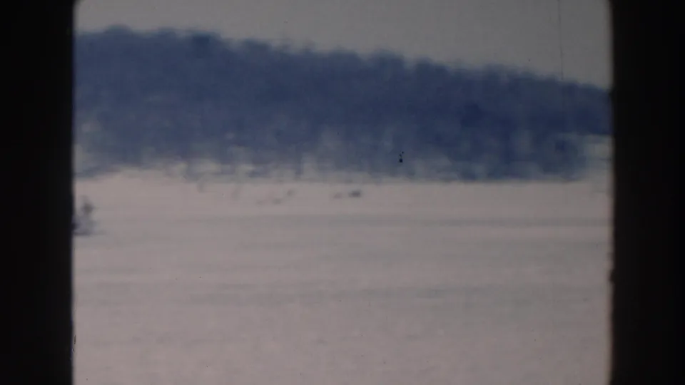 Soft 8mm frame from Tustin, Wisconsin, showing people scattered across a frozen lake in winter light.