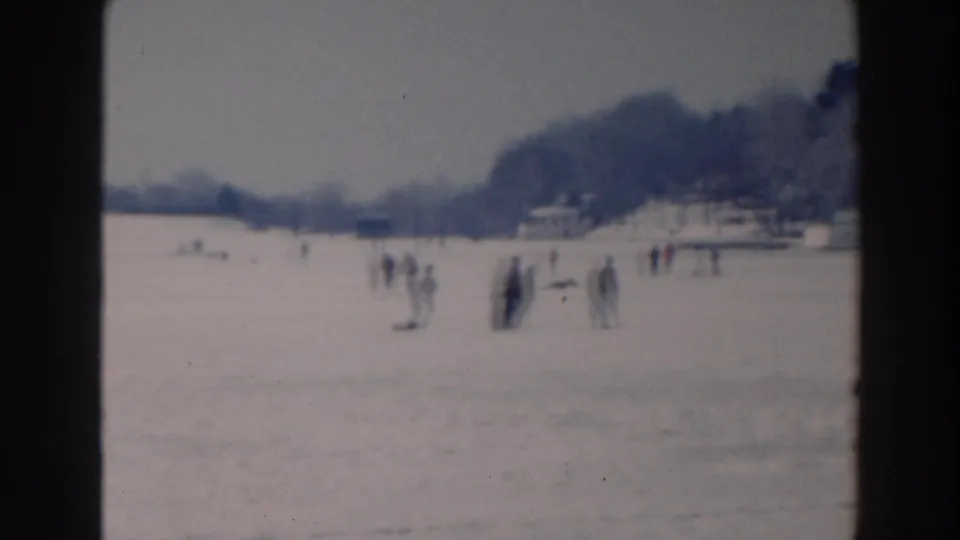 1964 Tustin, Wisconsin frame showing several people on lake ice near a distant shoreline and winter trees.