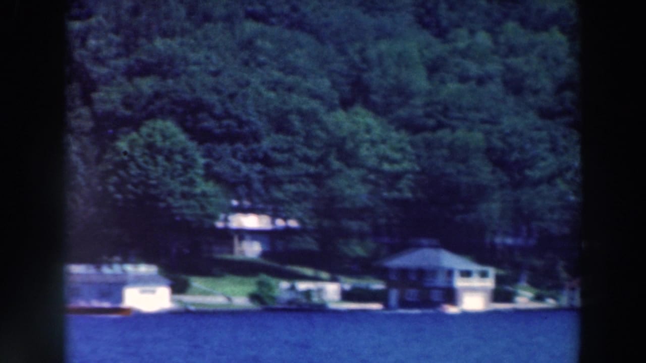 Wooded lakeshore with several homes across blue water.