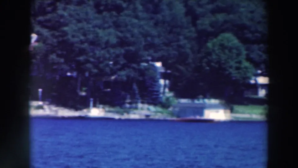 A home-movie view across a Wisconsin lake toward trees, shoreline structures, and distant lakeside homes.