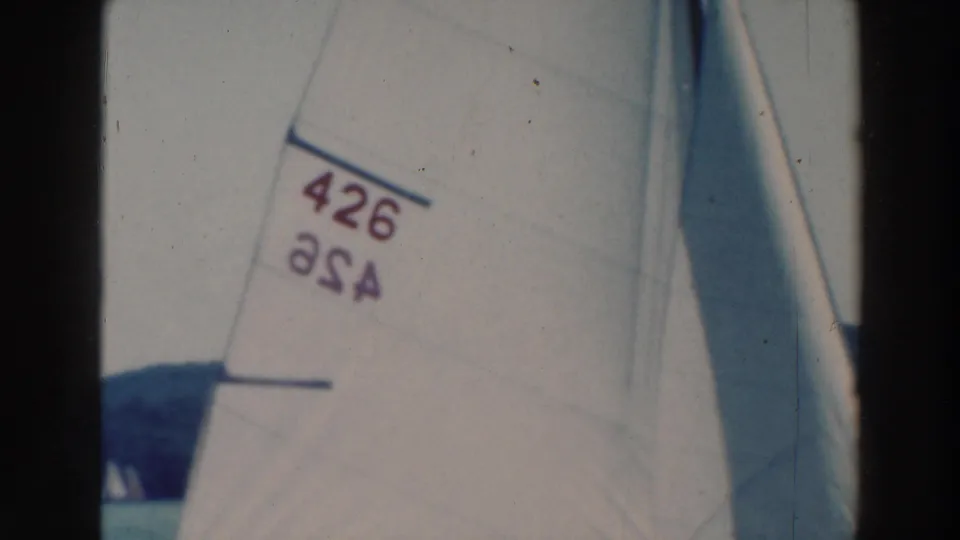Close 1964 lake-sailing frame with a white sail marked 426, partially cropped by the home-movie camera.
