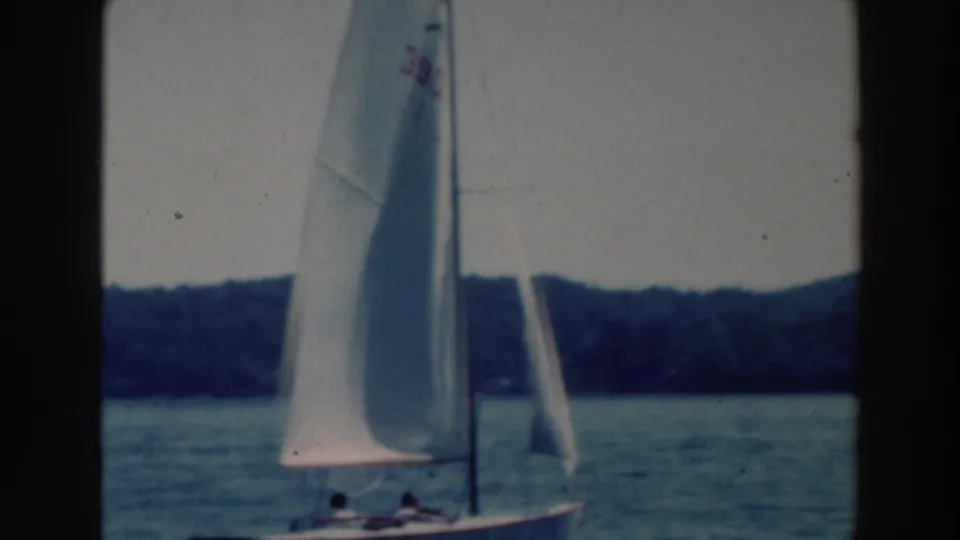 1964 Wisconsin 8mm frame showing a sailboat under white sail with another sail partly visible beyond it on the lake.