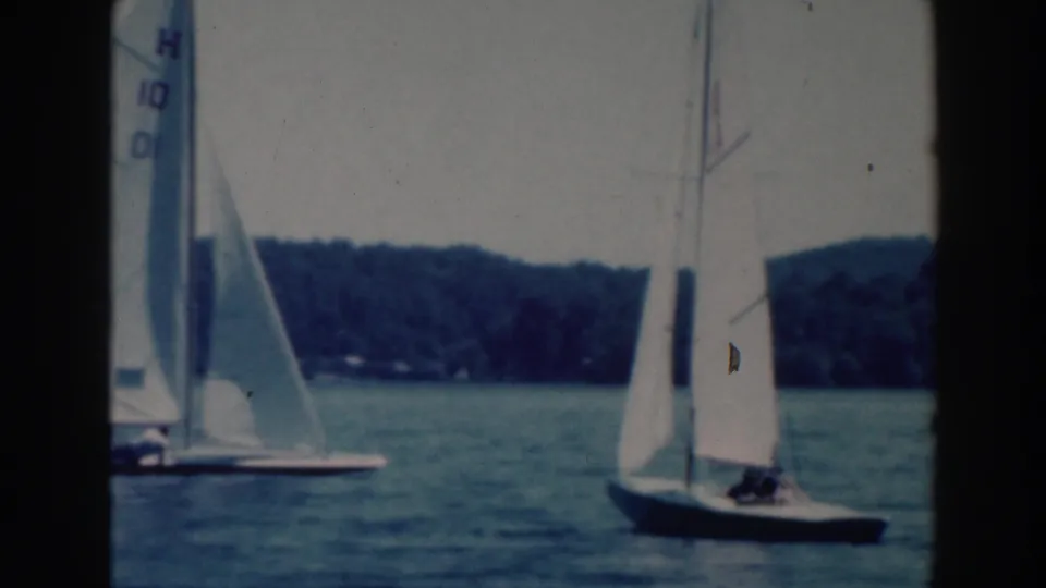 1964 Tustin, Wisconsin 8mm frame showing several small sailboats on a lake, including a numbered white sail near the left edge.