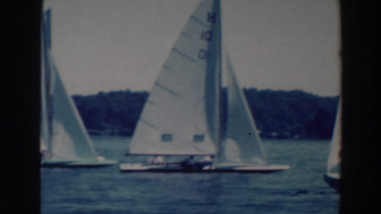 1964 Tustin, Wisconsin lake scene with multiple small sailboats and visible sail numbers against a wooded shore.
