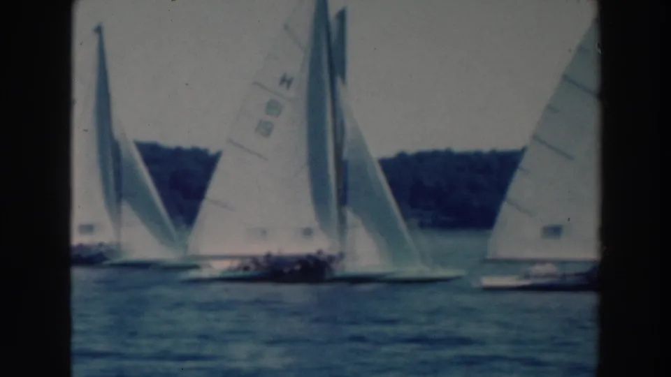 1964 Tustin, Wisconsin 8mm frame with close white sails, distant boats, lake water, and wooded shoreline.