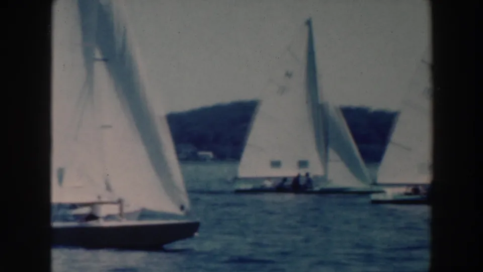 1964 Tustin, Wisconsin lake footage showing a foreground sailboat with other numbered sails and tiny sailors in the background.